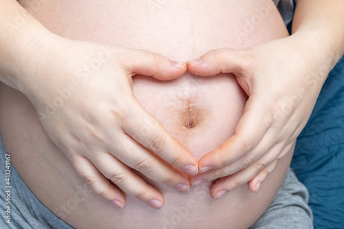 The concept of pregnancy. Pregnant woman making a heart shape with her hands on her belly. A pregnant woman is expecting a baby. Pregnancy, motherhood, people, love and expectation concept © Alena