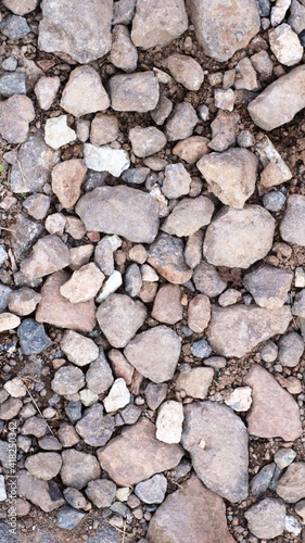 rocky natural surface of a mixture of different stones and sand, top view, cobblestones and pebbles scattered on the ground, fragments of stone rocks of gray-beige shades