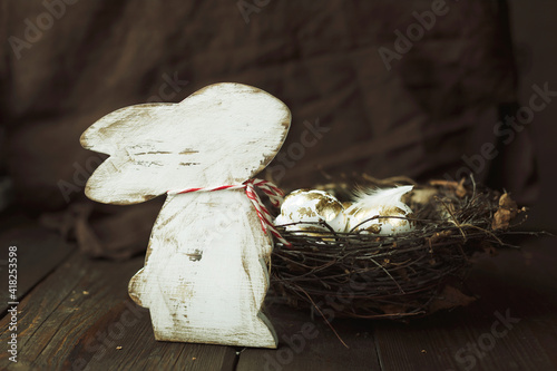 easter background with bunny figure and golden easter eggs in a nest on a dark wood background in vintage style