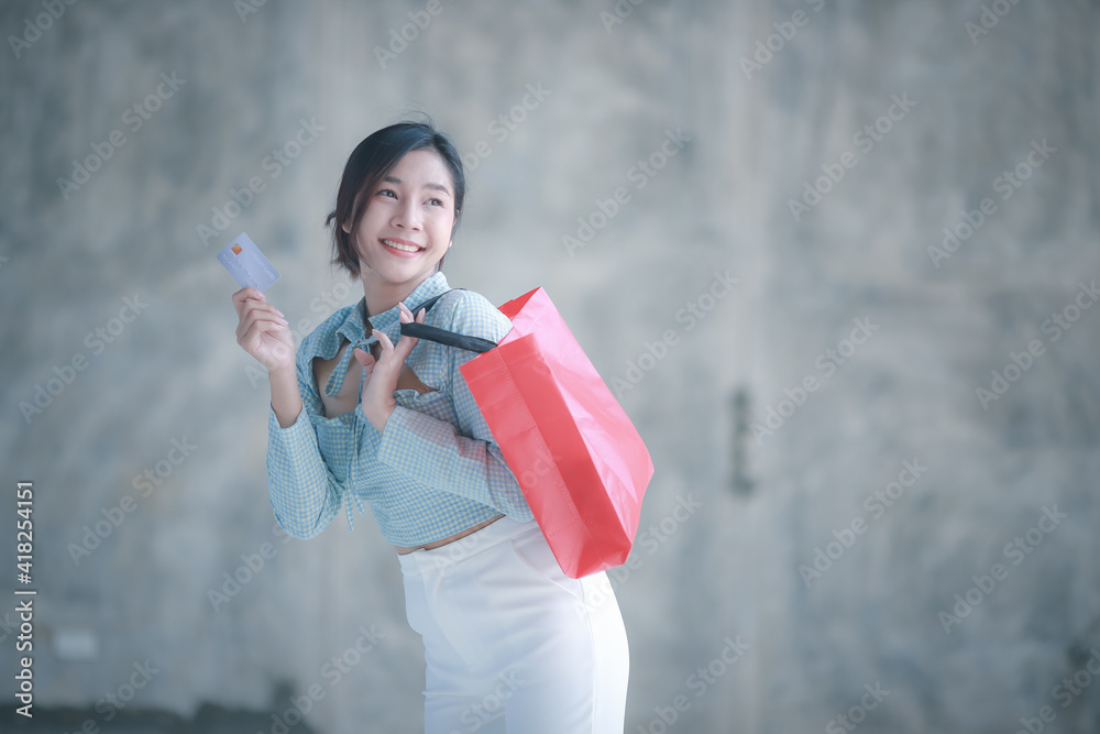 Beauty consumer woman carrying a shopping bag.Portrait of beautiful Asian woman wearing Casual wear showing credit card and smartphone with a shopping bag in hand on gray background,shooping concept Beauty consumer woman carrying a shopping bag.Portrait of beautiful Asian woman wearing Casual wear showing credit card and smartphone with a shopping bag in hand on gray background,shooping concept