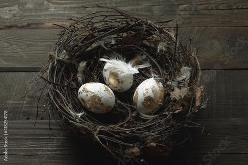 easter background with golden eggs in a nest and feathers on wood background