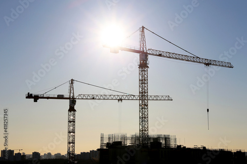 Construction cranes and unfinished residential building on blue sky and sunshine background. Housing construction, apartment block in city