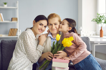 Portrait of three generations of women, mom, grandma and granddaughter celebrating event. Girl with mother congratulating grandmother on birthday, March 8 or Mother's Day handing gifts and flowers.
