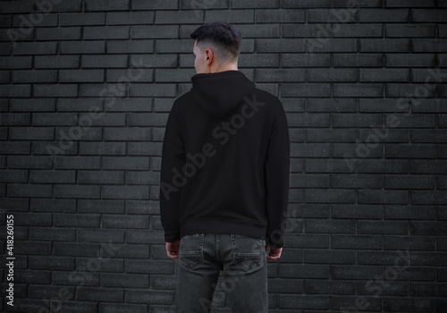 Тemplate of black men's clothing with long sleeves on a young guy on a brick wall background, back, sweatshirt with a hood. © olegphotor