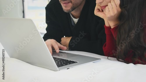 Man and woman couple in casual winter outfit lay down on bed using laptop with happy and romantic mood in bedroom