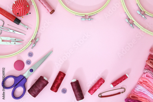 Composition with sewing accessories on a pink background with needles, a spool of thread, scissors and a measuring tape