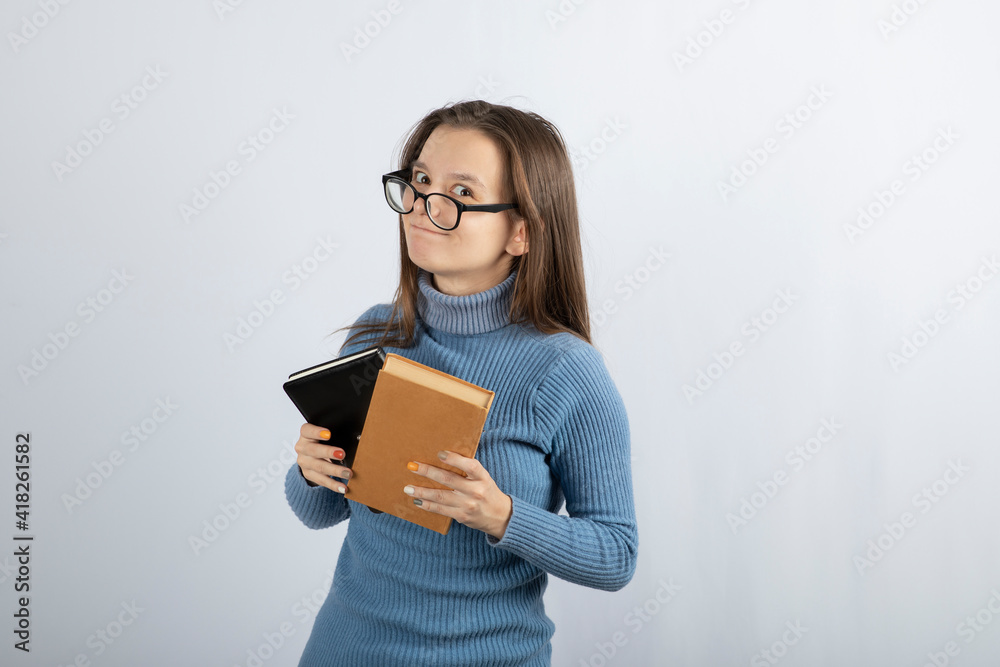 Portrait of a girl in eyeglasses holding two books on white-gray background Portrait of a girl in eyeglasses holding two books on white-gray background