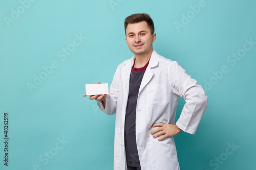 Doctor in a white coat holds a business card in his hand isolated on a blue background.