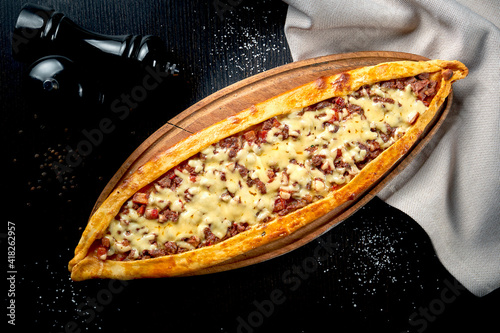 Turkish pide dish with slices of beef, tomatoes and cheddar cheese on black background