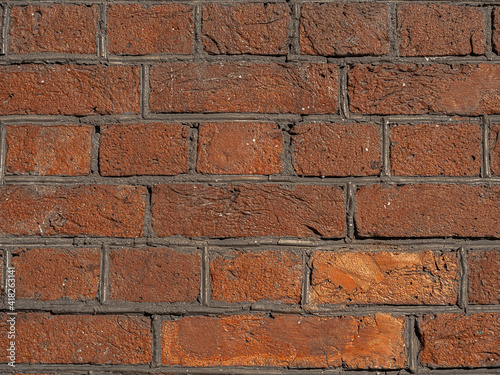 Brickwork made of red orange shine golden geometric horizontal bricks bonded with cement grout between square stones. Wall exterior. Build concept