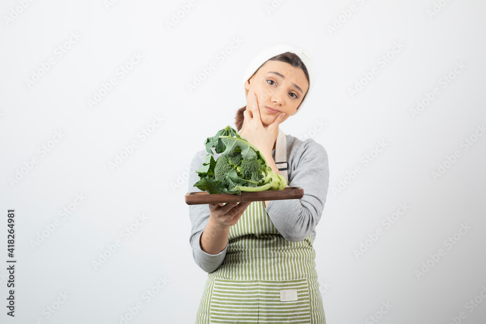 Picture of a pensive attractive woman holding a wooden plate of broccoli Picture of a pensive attractive woman holding a wooden plate of broccoli