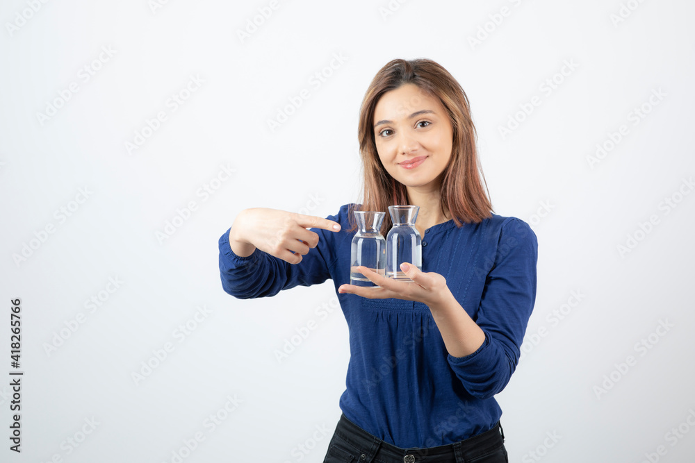 Beautiful woman in blue blouse holding glass of water and pointing at it Beautiful woman in blue blouse holding glass of water and pointing at it