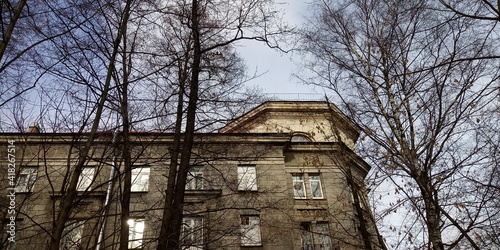 Fragment of a residential building with a turret and bare trunks and branches of trees in early spring  © HelenkaNNN