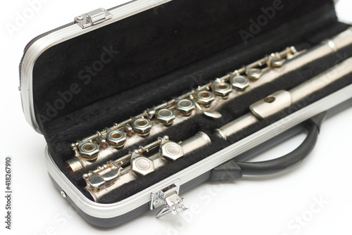 Partial side view of shiny disassembled silver flute in black case against white background