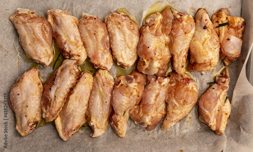 Raw chicken wings marinated with oil, pepper, chives, honey and spices on a baking tray.