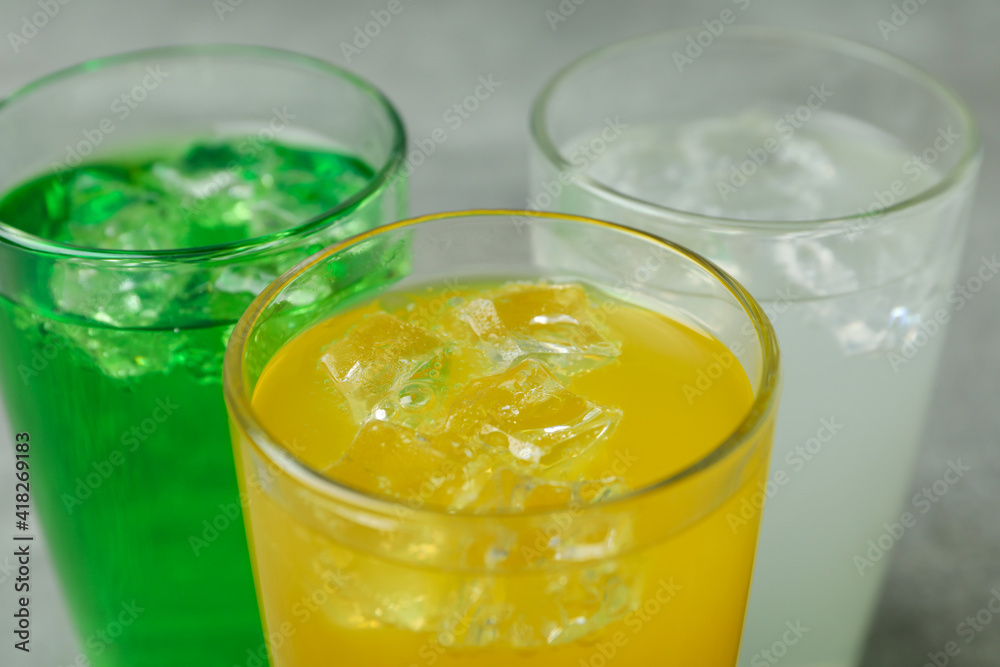 Glasses of different soda on gray background, close up Glasses of different soda on gray background, close up