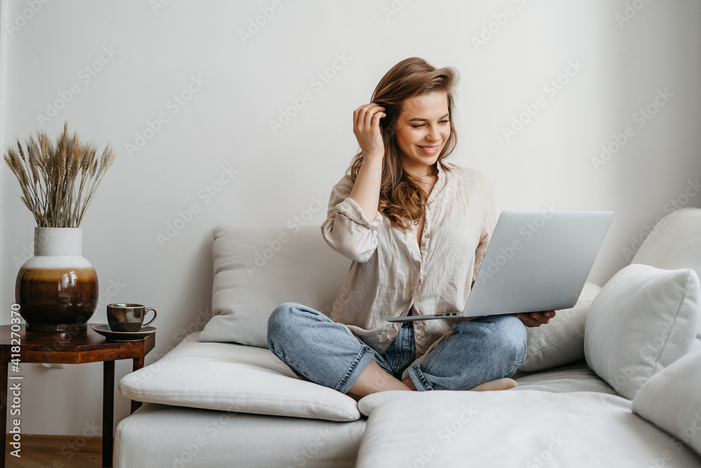 Portrait of a young female freelancer sitting on the couch and using laptop at home happily Portrait of a young female freelancer sitting on the couch and using laptop at home happily