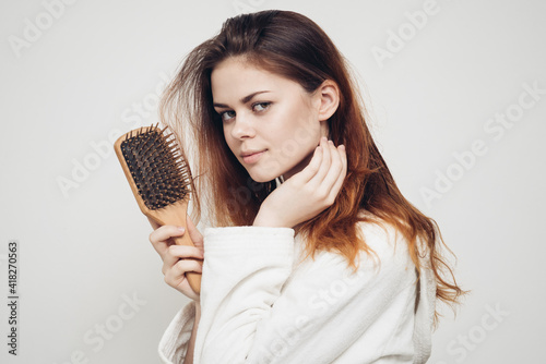 woman with a comb in her hand and in a white robe on a light background and hair loss
