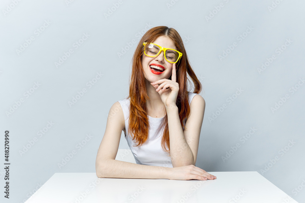 red-haired woman sitting at a table wearing yellow glasses smile red lips model red-haired woman sitting at a table wearing yellow glasses smile red lips model