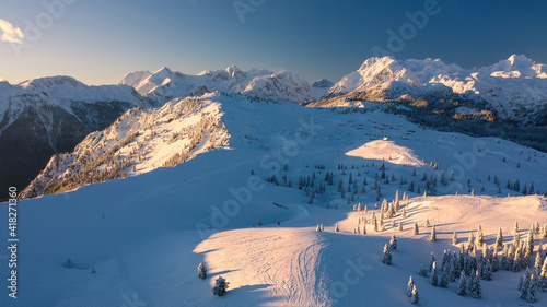 Aerial view of winter landscape with snow covered forest in the mountains with beautiful sunset light.