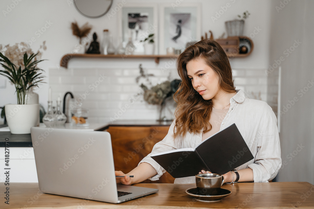 Young woman takes notes in front of laptop at home. Working from home. Concept of education and communication. Young woman takes notes in front of laptop at home. Working from home. Concept of education and communication.