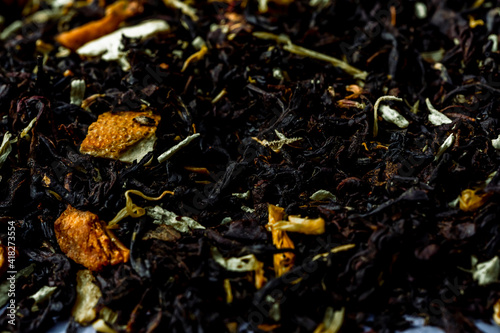 Dry black tea leaves with pieces of dried citrus peel, fruit and flowers. Close up tea background background.
