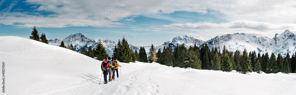 Friends practicing snowshoe trekking in the snowy mountains. Dolomites, Italy. 