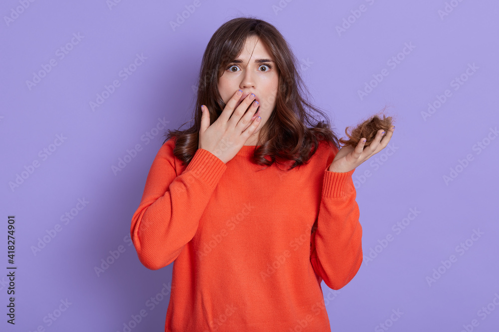 Beautiful European woman holding loosing hair, looks scared and amazed, covering opened mouth for surprise, disbelief face, looking at camera with big eyes, has problem with hair, hair loos. Beautiful European woman holding loosing hair, looks scared and amazed, covering opened mouth for surprise, disbelief face, looking at camera with big eyes, has problem with hair, hair loos.