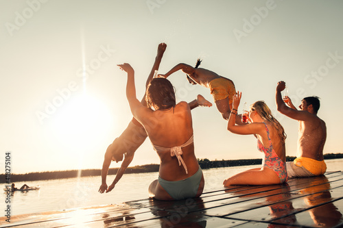 Young friends having fun enjoying a summer day swimming and jumping at the lake. 