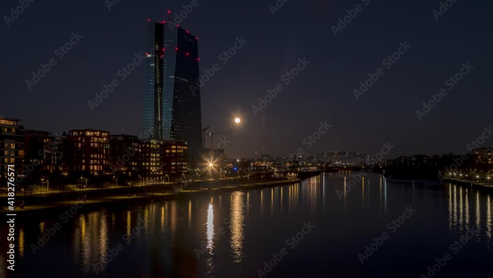 Time-lapse of the rising full moon in Frankfurt with the river Main, some bridges and the European Central Bank with its tall building in the background at night in winter. Time-lapse of the rising full moon in Frankfurt with the river Main, some bridges and the European Central Bank with its tall building in the background at night in winter.