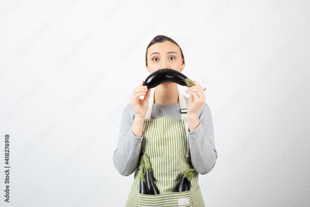 Image of beautiful housewife having eggplants in apron and showing one Image of beautiful housewife having eggplants in apron and showing one