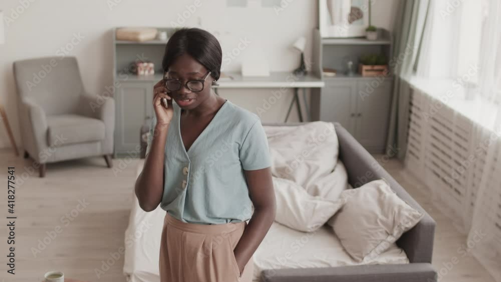 Medium shot of young attractive African-American woman wearing comfortable clothes and eyeglasses having important business call Medium shot of young attractive African-American woman wearing comfortable clothes and eyeglasses having important business call