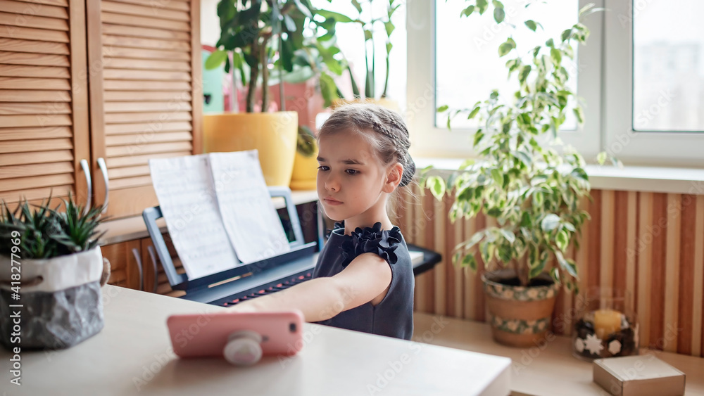 Pretty young musician in classic black dress playing digital piano at home during online concert and recording video, social distance during quarantine, online education concept, video blogging Pretty young musician in classic black dress playing digital piano at home during online concert and recording video, social distance during quarantine, online education concept, video blogging