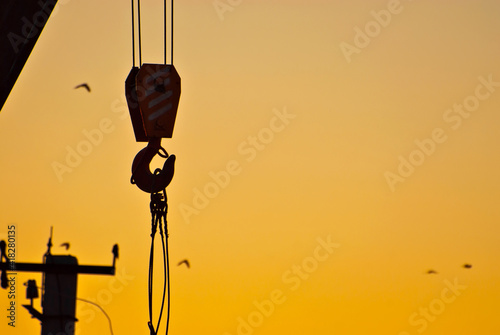 Silhouette of a crane on a background of sunset. Ropes and hooks on an orange background.