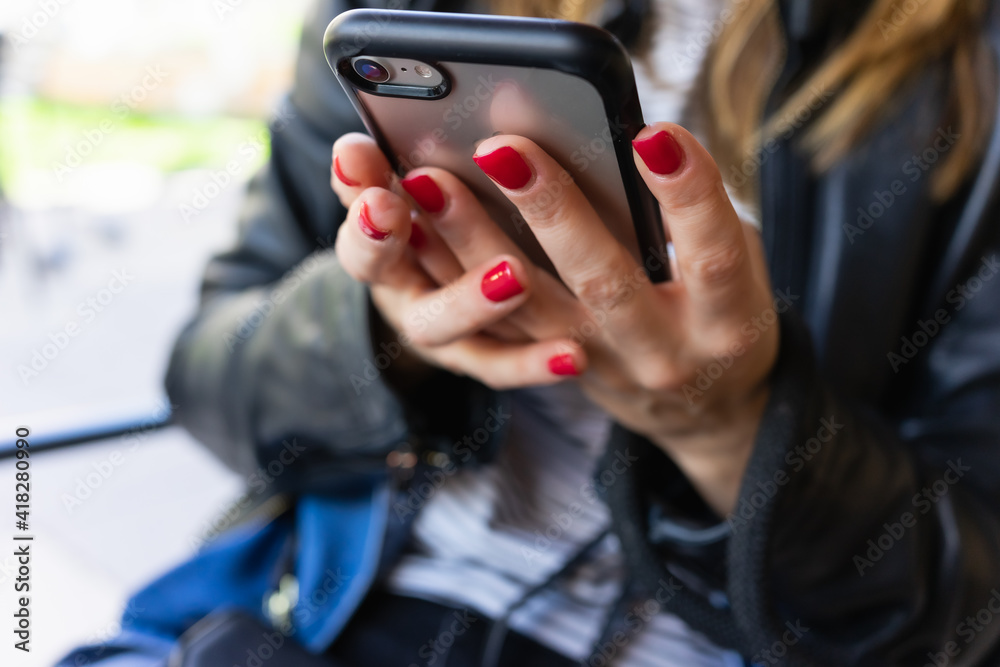 Caucasian woman with painted nails uses her mobile phone in a close-up with bokeh.