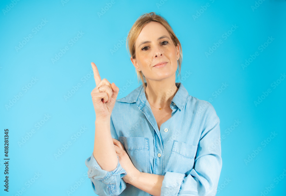 Portrait of a young woman dressed in casual shirt pointing finger up at copy space isolated over blue background