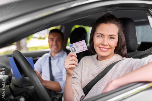 driver courses, exam and people concept - young woman with license and driving school instructor with clipboard in car