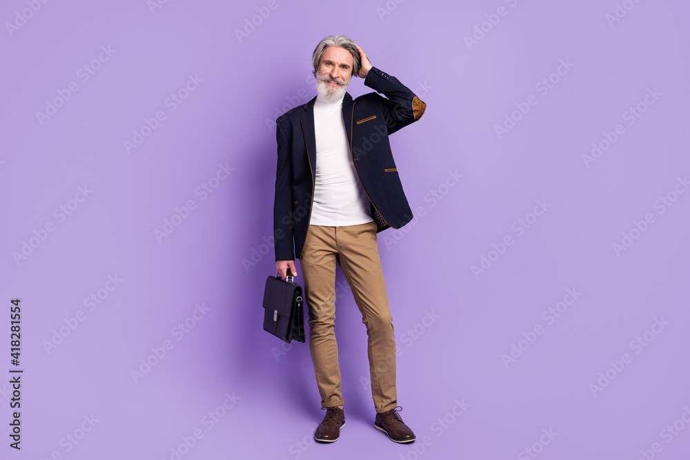 Full length photo of attractive pretty retired man formalwear walking arm head holding suitcase isolated violet color background Full length photo of attractive pretty retired man formalwear walking arm head holding suitcase isolated violet color background