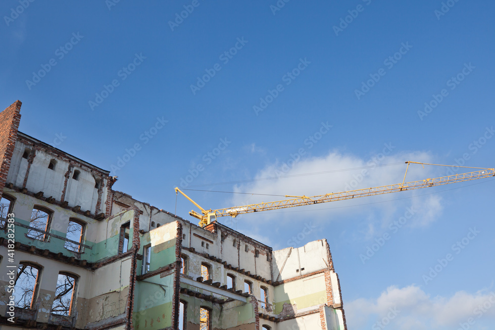Fragment of a partially demolished building against the sky and a crane, city.