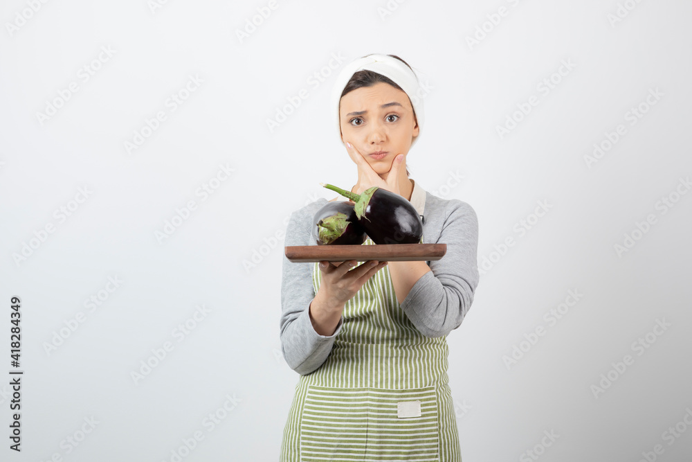 Portrait of female cook holding plate of big eggplants and thinking Portrait of female cook holding plate of big eggplants and thinking
