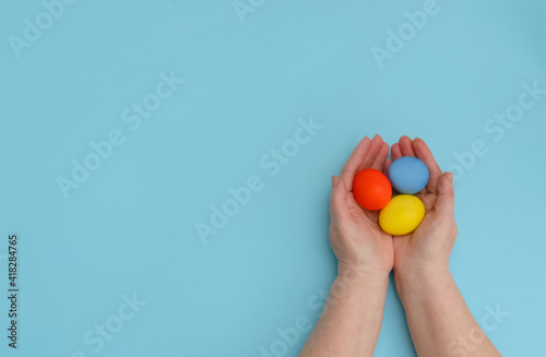 Happy Easter day.Colorful Easter eggs in the hands of an old lady on a blue background close-up.Greeting card or baner for your website or store sale.Flat lay.Copy space