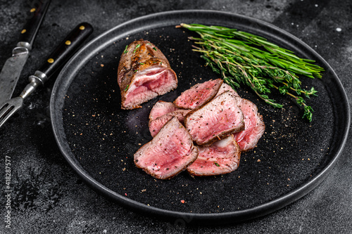 BBQ Grilled sliced lamb tenderloin meat steak on a plate. Black background. Top view