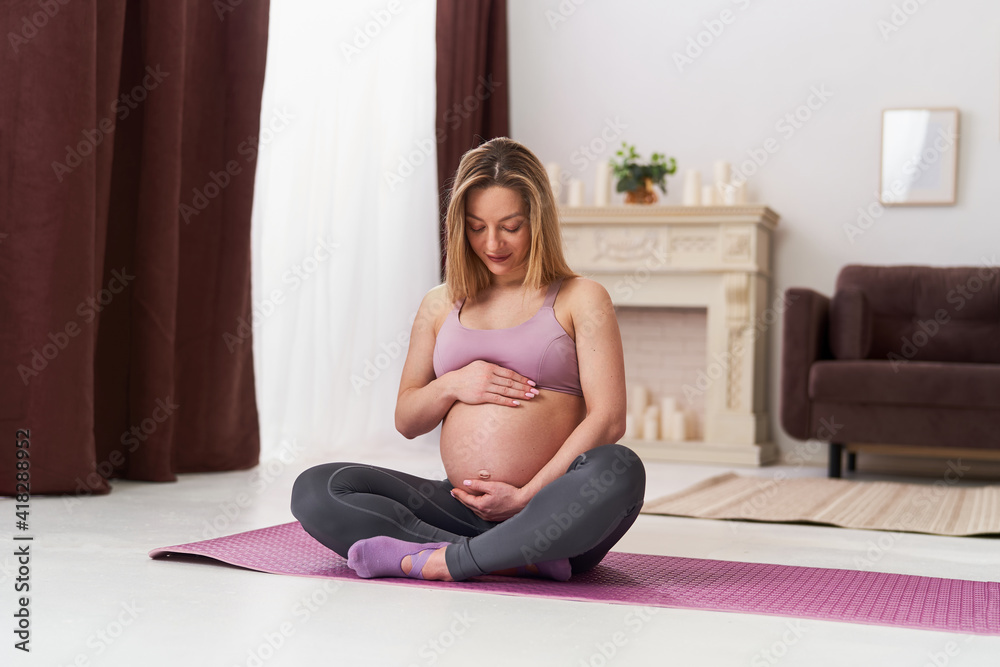 calm, attractive pregnant woman in sportswear practices yoga on a yoga mat, at home in the living room. health during pregnancy. yoga classes at home. Motherhood, harmonious pregnancy.