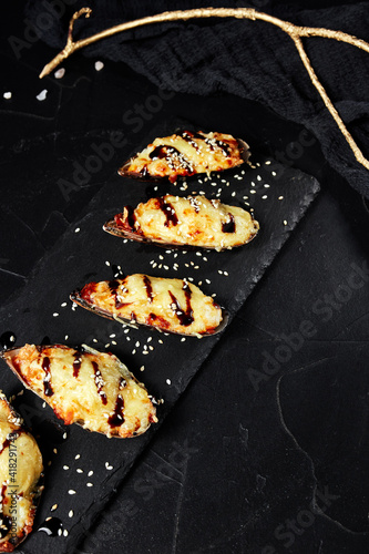 baked oysters on a black board on a dark background with a golden sprig