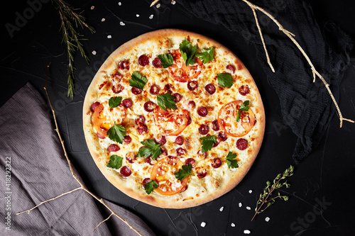 pizza on black textured background with dark napkin and golden sprigs top view