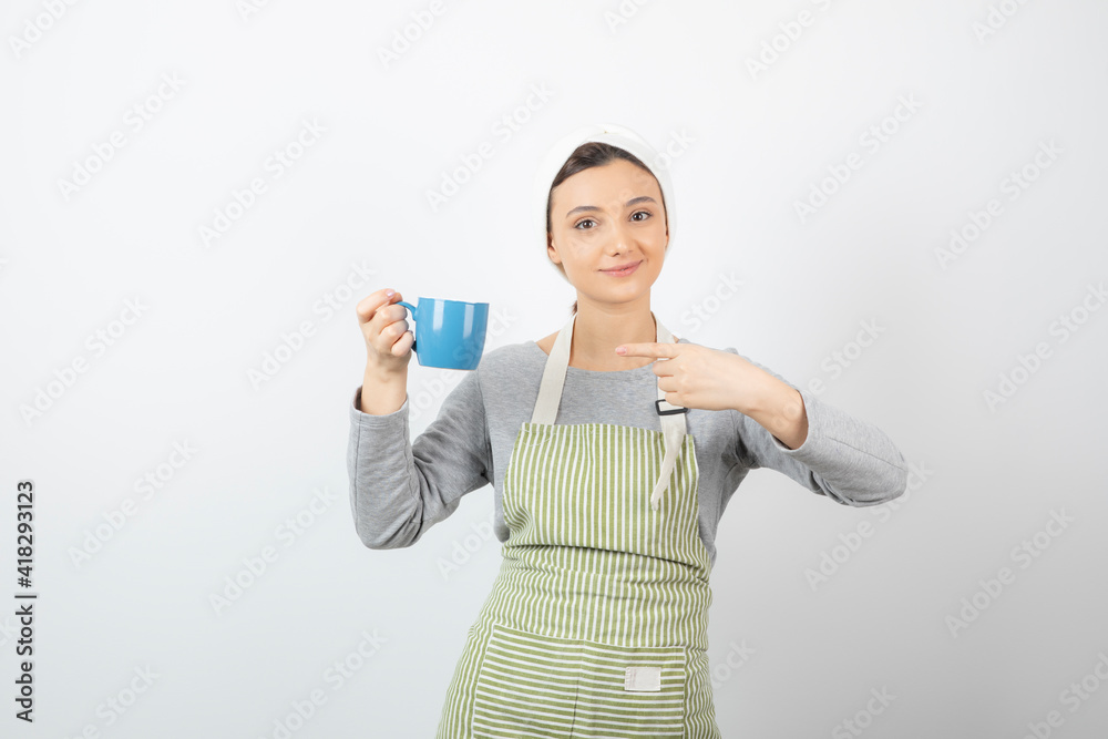 Image of a smiling young woman in apron pointing at a blue cup Image of a smiling young woman in apron pointing at a blue cup