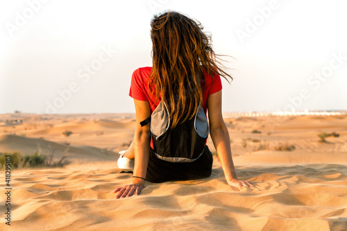 A girl from behind sitting on the desert sand. Perfect shot for travel and vacations.