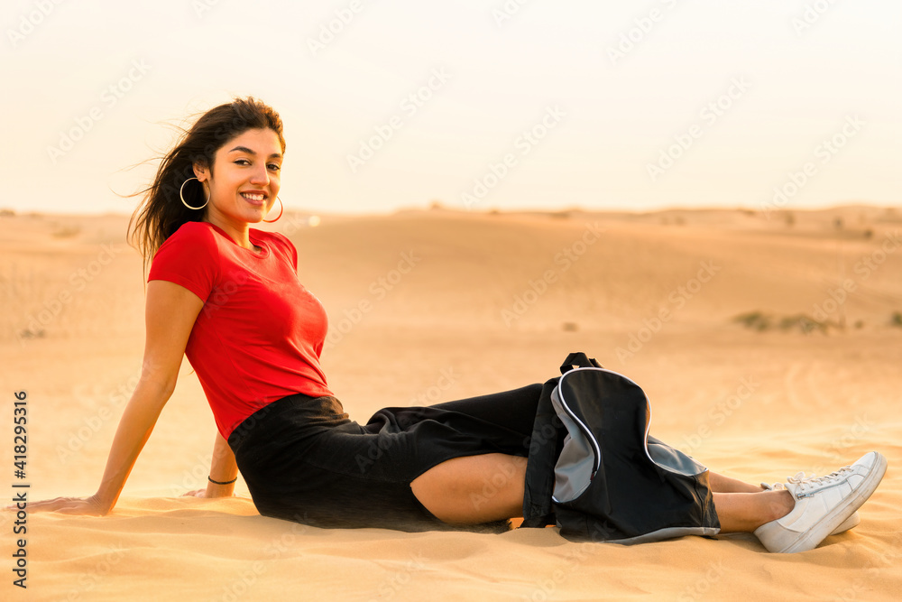 A girl in a red T-shirt and backpack is resting on the desert sand. Perfect shot for travel and vacations.