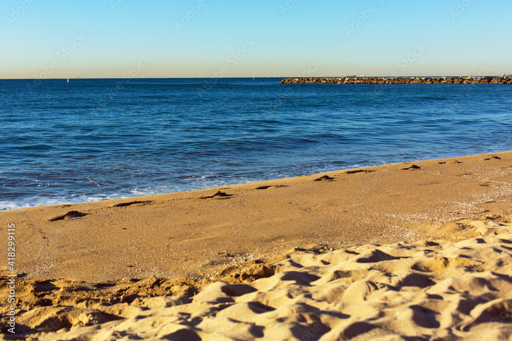 Coastal strip of the Mediterranean Sea with breakwaters and a sandy beach in the San Martí area in Barcelona, Spain