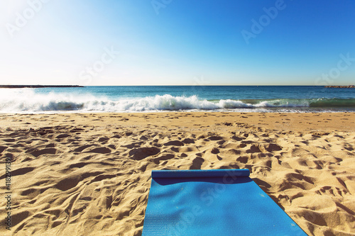 Fototapeta Naklejka Na Ścianę i Meble -  Blue yoga mat is on a sandy beach by the sea. Barcelona, Spain